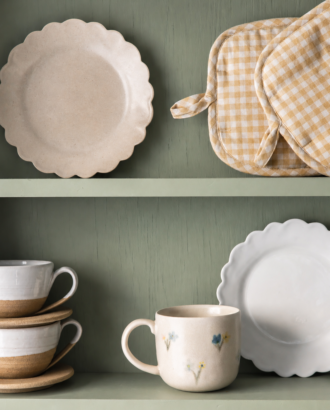 Ceramic plates, mugs, and checkered potholders on a green shelf.